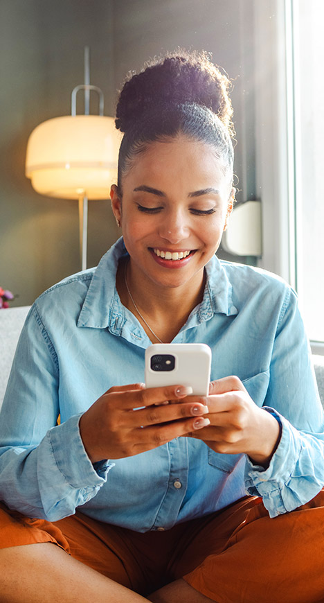 A young woman sitting with her legs criss-cross and smiling at her smartphone